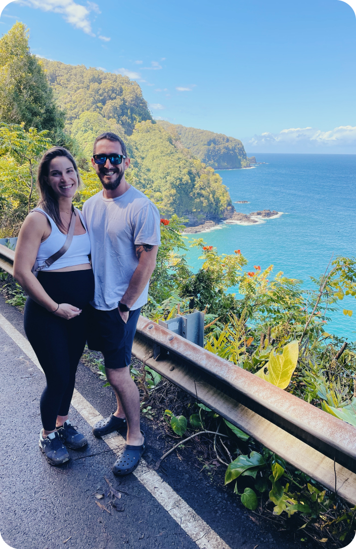 Expecting couple on a scenic mountain walk, with a beautiful sea backdrop, woman pregnant and smiling