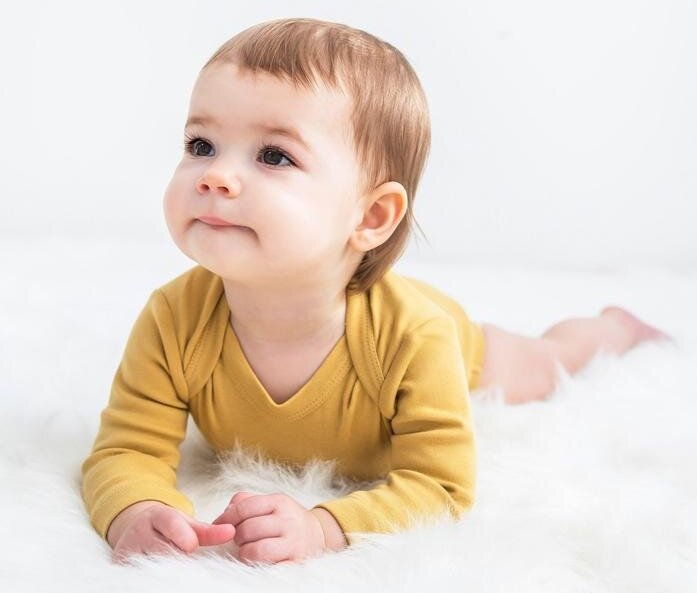 Adorable baby girl in a yellow organic cotton bodysuit, smiling and comfortable