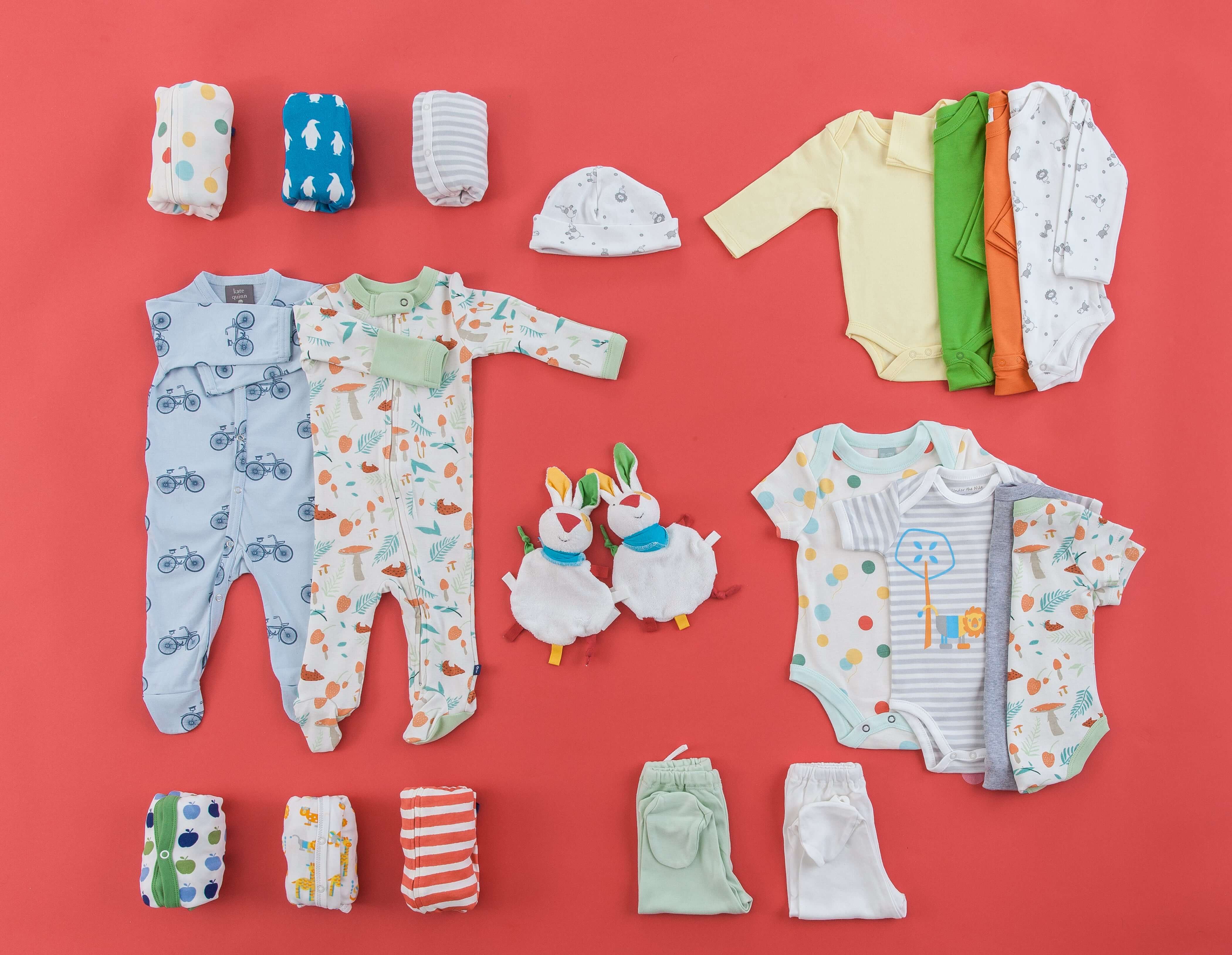 Playful baby clothing set with bodysuits, footies, hats, toys, and pants on a vibrant red background
