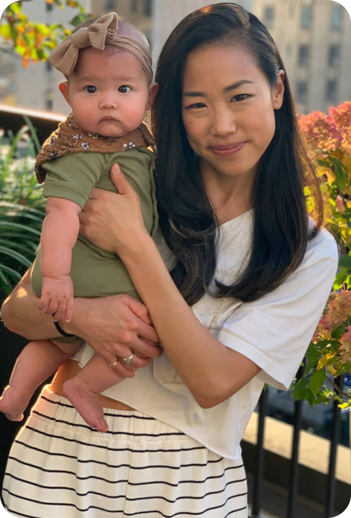 A mother holding her daughter in her arms in a garden, smiling at the camera